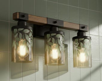 May include: A three-light vanity fixture featuring a horizontal dark wood beam with matte black metal accents. Each light has a cylindrical glass shade with a green leaf pattern and a warm-toned gradient, housing a single glowing light bulb.