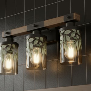 May include: Three-light vanity fixture with a wooden beam and black metal accents. Each light has a cylindrical glass shade with a leaf pattern and a warm-toned bulb. The fixture is mounted on a black tiled wall.