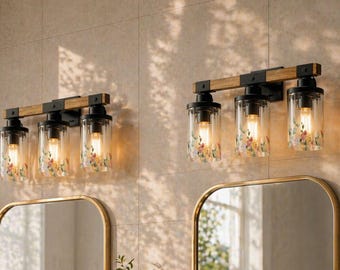 May include: Two wall-mounted vanity light fixtures, each featuring a horizontal wooden bar with black metal accents and three cylindrical glass shades. The glass shades are decorated with a colorful floral pattern and contain glowing light bulbs.