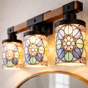 May include: A three-light vanity fixture with stained glass shades. The fixture has a wooden beam and black metal accents. The shades feature a floral design in pastel colors, including pink, blue, and green. The fixture is mounted above a round mirror.