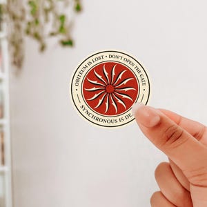 May include: A round sticker with a red and cream design. The center features a sunburst pattern. The sticker has the phrases "OBITEUM IS LOST", "DON'T OPEN THE GATE", and "SYNCHRONOUS IS DEAD" printed around the edge.