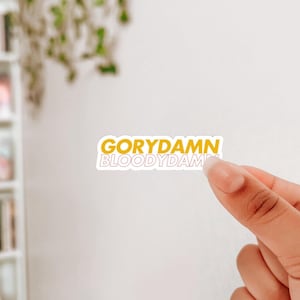 Puede incluir: Una pegatina amarilla con el texto "GORYDAMN BLOODYDAMN" en letras blancas.