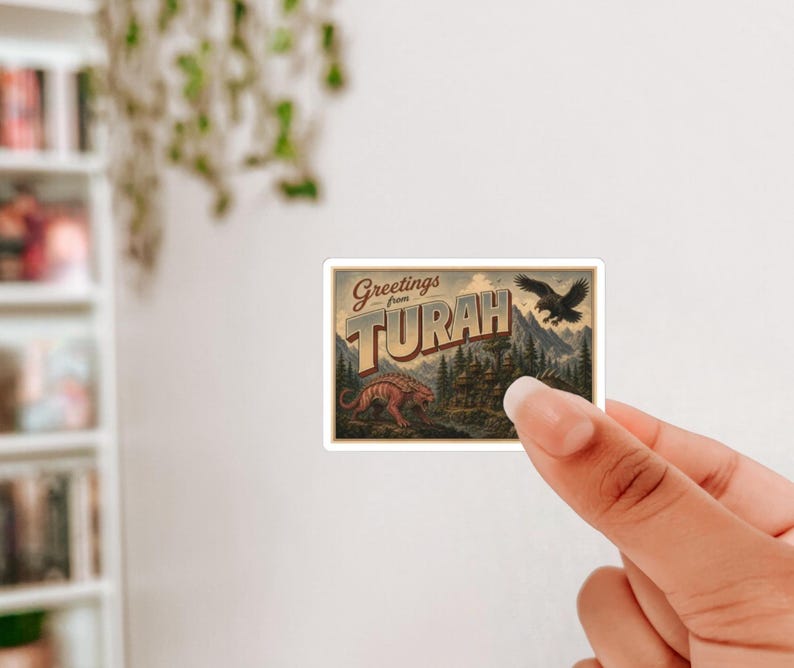 May include: A sticker featuring a vintage postcard design with the text "Greetings from Turah." The illustration includes a dinosaur, an eagle, and a mountain landscape, with a sepia-toned color scheme.