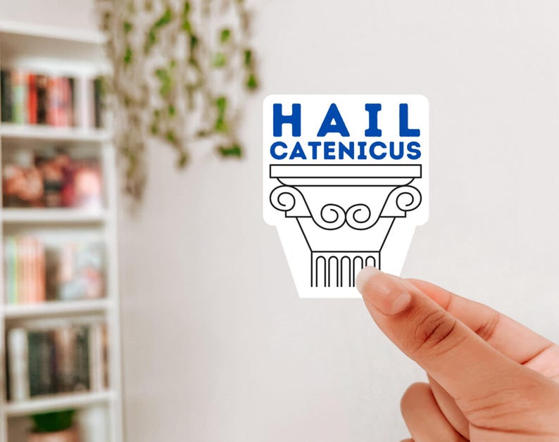 Op de afbeelding: Een witte sticker met de tekst "HAIL CATENICUS" in blauw en zwart. De sticker heeft een zwart-wit illustratie van een klassieke zuil. De sticker wordt door een hand vastgehouden.