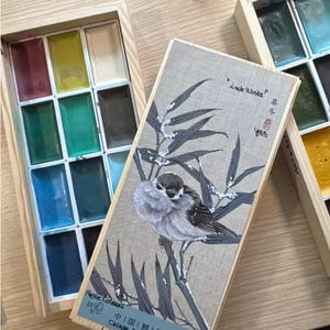 May include: Wooden watercolor paint set with a lid featuring a bird illustration. The set includes a variety of colorful paints in rectangular pans. Text on the lid reads "Little Winter" and "Chinese painting colors".