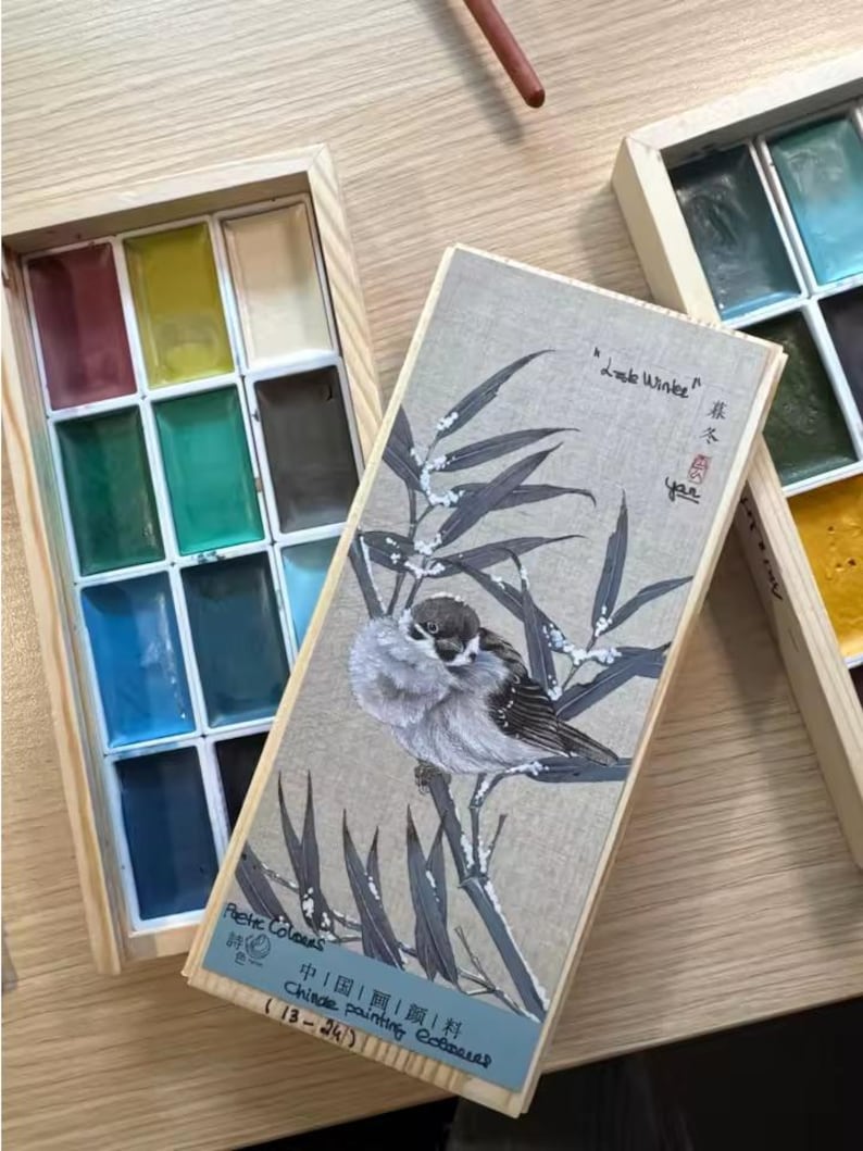 May include: Wooden watercolor paint set with a lid featuring a bird illustration. The set includes a variety of colorful paints in rectangular pans. Text on the lid reads "Little Winter" and "Chinese painting colors".