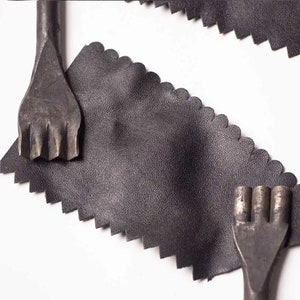May include: Two black leather pieces with a scalloped edge. Each piece has a metal tool with multiple prongs on top.