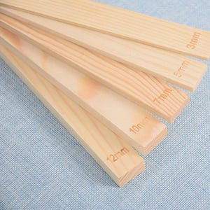 May include: Five wooden strips of varying widths, labelled with their measurements in millimetres: 3mm, 5mm, 7mm, 10mm, and 12mm. The strips are arranged in a fan shape, with the widest strip at the bottom and the narrowest strip at the top.