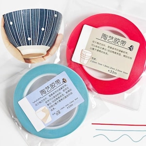 May include: A ceramic bowl with a blue and white striped design and white dots is held in a hand. Two rolls of masking tape are visible, one red and one light blue, with text in Chinese characters. The tape widths are 0.5mm to 3mm.