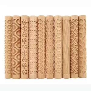 Puede incluir: Una colección de diez rodillos de madera con varios diseños en relieve. Los diseños incluyen flores, olas, copos de nieve y hojas. Los rodillos son de madera clara y están dispuestos verticalmente.