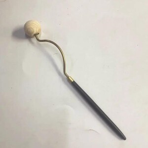 May include: A wooden facial roller with a light-coloured, spherical head. The roller has a curved, brass-coloured metal stem and a dark, cylindrical handle. The handle is connected to the stem with a gold-coloured metal piece.