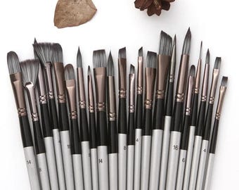 May include: A collection of artist paint brushes with black handles and silver ferrules. The bristles vary in shape and size, with some angled and others flat. The brushes are arranged on a white surface, with a pinecone and leaf in the background.