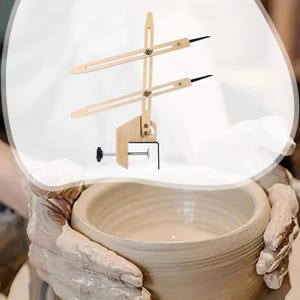 Puede incluir: Un calibrador de cerámica de madera con brazos ajustables y puntas negras. La herramienta se sujeta a un cuenco de cerámica, probablemente para medir o dar forma a la cerámica. El calibrador es de madera clara.