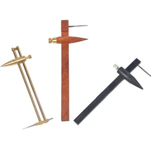 May include: Three marking gauges for woodworking. One is made of brass with two parallel rods and a pointed tip. The second is a wooden gauge with a central pointed adjustment knob. The third is a black plastic gauge with a pointed metal scribe.
