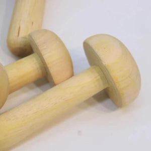 May include: A collection of three light-colored wooden mushroom-shaped objects. Each piece features a smooth, rounded cap attached to a cylindrical stem, showcasing the natural grain and pale beige tones of the unfinished wood material.