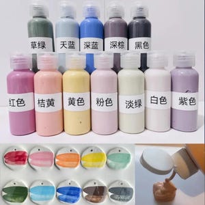 Puede incluir: Una colección de botes de pintura en varios colores, incluyendo verde, azul, morado y rosa, con etiquetas en caracteres chinos. Debajo, muestras de color pintadas en forma circular. Se está abriendo un bote, revelando la pintura.