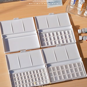 Puede incluir: Cuatro paletas de pintura de acuarela de plástico blanco con tapas. Cada paleta tiene 24 pocillos de pintura individuales.