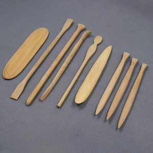 May include: A collection of light-colored wooden tools, including various sizes of spatulas and rounded tools, arranged on a gray surface. The tools have a natural wood grain and are likely used for crafting or cooking.