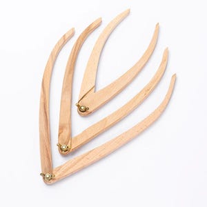 May include: A collection of wooden compasses, each with a curved, slender design. The compasses are made of light-colored wood and feature brass hardware at the joints. The background is plain white.