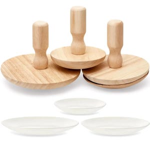Puede incluir: Un conjunto de utensilios de cocina de madera y platos de cerámica blancos. Los artículos de madera incluyen tres platos redondos de madera de color claro con asas adjuntas. También se ven tres platos blancos, poco profundos y de forma ovalada.