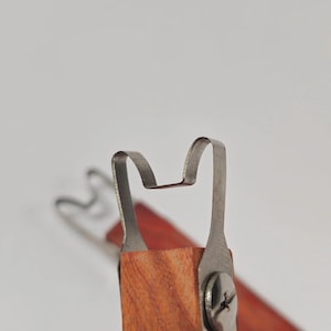 May include: Close-up of a metal tool with a curved, hook-like end attached to a wooden handle. The tool has a silver finish and is secured with a screw. The wooden handle is a warm, reddish-brown colour.