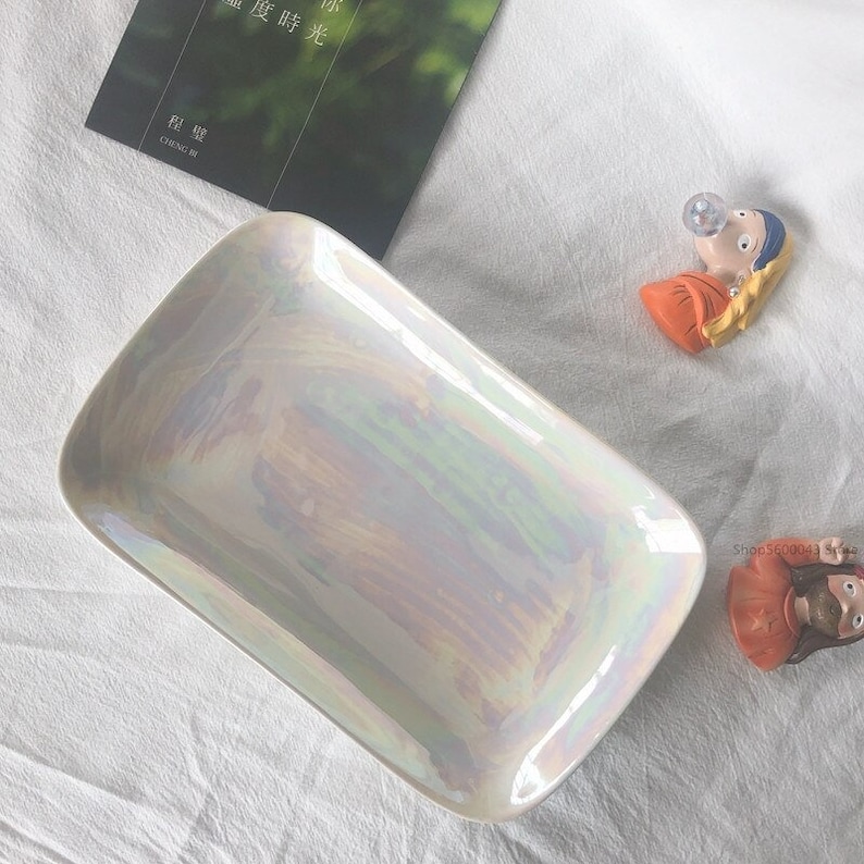May include: A rectangular iridescent white ceramic serving dish with rounded edges. The dish is on a white surface.
