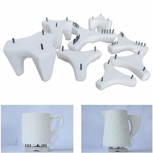 Könnte beinhalten: Weiße Keramik-Ofenstifte in verschiedenen Formen und Größen, die zum Abstützen von Keramik beim Brennen bestimmt sind. Das Bild zeigt auch eine weiße Tasse und einen Krug, die jeweils auf einem Stift ruhen. Die Stifte haben dunkelgraue Stifte.
