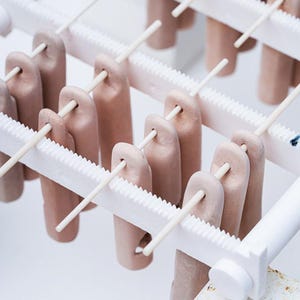Peut inclure: Gros plan sur un moule à sucettes glacées avec plusieurs sucettes glacées brun clair sur des bâtonnets en bois. Les sucettes glacées sont dans un moule en plastique blanc avec un design en crête. Le fond est blanc.