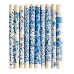 May include: Ten cylindrical rolling pins arranged side by side, each featuring a unique blue ink pattern on a light cream background. Designs include floral motifs, swirling vines, small red hearts, geometric lace, and a dragon illustration.