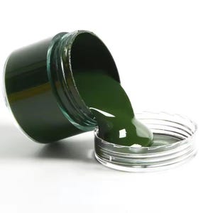 Puede incluir: Pintura verde siendo vertida de un frasco a un contenedor transparente.