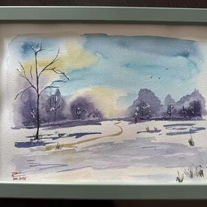 May include: Watercolor painting of a winter landscape in a green frame. The artwork depicts a snowy scene with trees, a path, and a colorful sky with shades of blue, yellow, and purple. Signed and dated in the lower left corner.