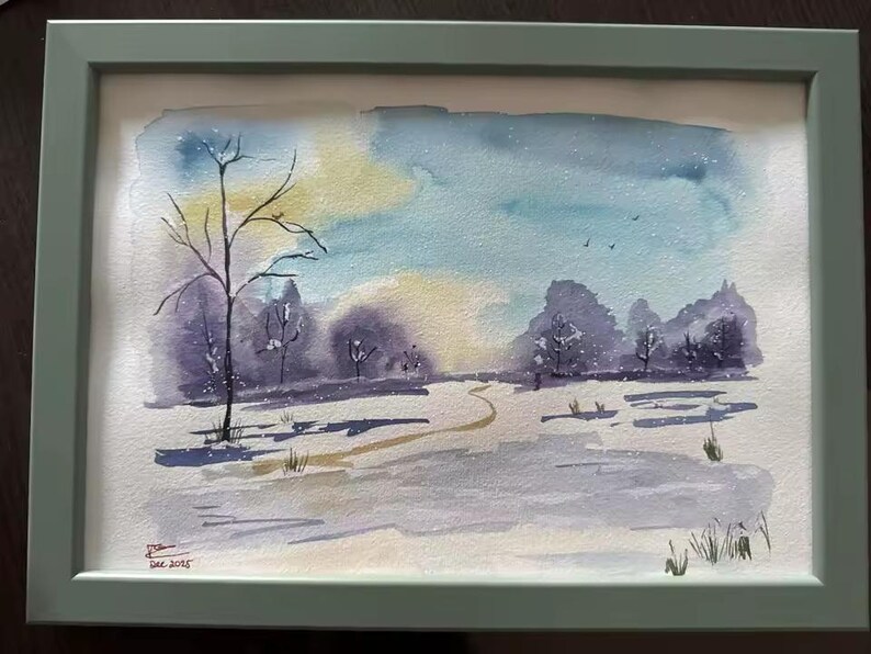 May include: Watercolor painting of a winter landscape in a green frame. The artwork depicts a snowy scene with trees, a path, and a colorful sky with shades of blue, yellow, and purple. Signed and dated in the lower left corner.