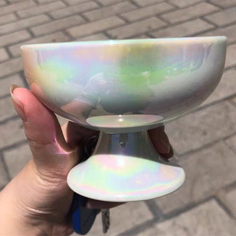 May include: A white iridescent ceramic bowl with a pedestal base. The bowl has a smooth, glossy finish and a pearlescent sheen.