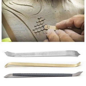 May include: Three metal sculpting tools for clay. The tools are silver, gold, and black. The tools are used to create patterns and designs in clay.