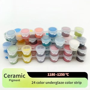 K&ouml;nnte beinhalten: Eine Sammlung von 24 Keramikpigmentfarben in kleinen, transparenten Kunststoffbeh&auml;ltern mit wei&szlig;en Deckeln. Die Beh&auml;lter sind auf transparenten Kunststoffschalen gestapelt. Der Text "Ceramic Pigment" und "24 color underglaze color strip" ist sichtbar.
