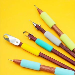 May include: A collection of wood-handled tools with various metal tips and colorful foam grips. The tools have dark brown wooden handles, with light green, yellow, gray, and blue foam grips. The tips include a small loop, a pointed tip, and a curved blade.