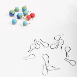 May include: A collection of small, colorful, round ornaments with a swirl pattern. The ornaments have silver jump rings attached. There are also several silver jump rings scattered on a white surface.