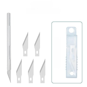 Może przedstawiać: Srebrny nóż rzemieślniczy z teksturowanym uchwytem i zestawem ostrzy zapasowych. Ostrza są ostre i kątowe, z małym otworem w pobliżu podstawy. Przezroczyste plastikowe etui zawiera dodatkowe ostrza.