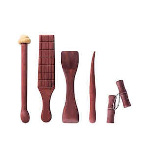 Peut inclure: Ensemble de cinq outils en bois pour la poterie, comprenant une côte, une palette, un outil à aiguille et deux outils de modelage. Les outils sont tous en bois rouge foncé.