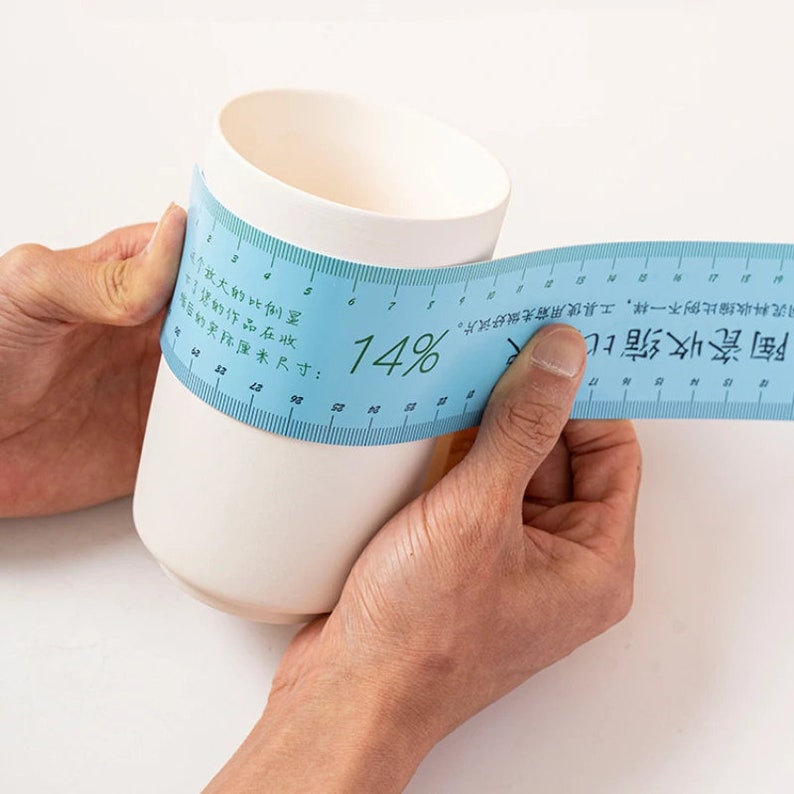 May include: A blue measuring tape with a white ceramic mug. The tape reads "Ceramic Shrinkage Ratio" and "14%".