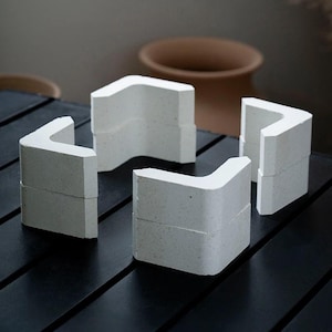 May include: Four white ceramic corner pieces, each with a slightly textured surface, arranged in a square shape on a black surface.