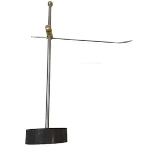 Op de afbeelding: Een metalen en messing sieraden display stand. De standaard heeft een donkere, rechthoekige basis, een verticale paal en een horizontale arm met een gebogen uiteinde. De bovenkant van de verticale paal heeft een kleine messing bal.