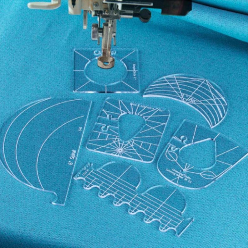 Peut inclure: Un ensemble de gabarits de couture en plastique transparent pour cr&eacute;er diff&eacute;rentes formes et motifs. Les gabarits sont dispos&eacute;s sur une surface en tissu bleu avec une aiguille de machine &agrave; coudre en arri&egrave;re-plan.