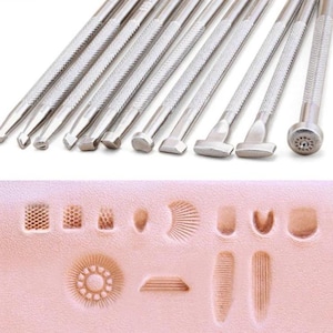 Op de afbeelding: Een set zilveren metalen leerstempels met getextureerde handgrepen. Hieronder worden verschillende gestempelde leerpatronen getoond, waaronder geometrische vormen en bloemmotieven. De tools zijn voor leerbewerking.