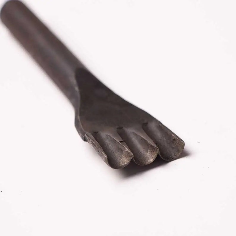 May include: A close-up of a black metal leather punch tool with four prongs. The tool is used to create holes in leather for stitching.