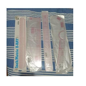 May include: A collection of pink and clear plastic rulers and templates, including a straight ruler, a curved ruler, and a French curve, on a blue and white striped surface. One ruler is labeled "Inch/Metric X-Ray".