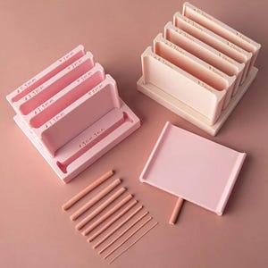 May include: A set of pink crafting tools, including a tray with a handle, several rods, and multiple tiered measuring guides labeled with millimeter measurements. The guides are labeled from 0.5mm to 5mm. The tools are arranged on a pink surface.