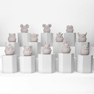 Puede incluir: Una colección de doce figuras de animales de color gris claro, cada una con características únicas, exhibidas sobre pedestales geométricos blancos. Las figuras incluyen un ratón, un cerdo, un conejo y otras criaturas, todas con un diseño minimalista.