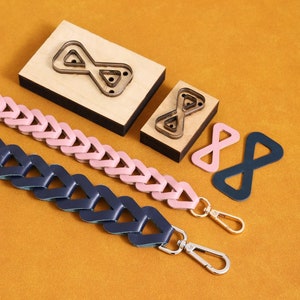 May include: Two leather straps with a chain link design, one pink and one blue, with metal clasps. Two wooden templates for cutting out infinity symbol shapes are also shown.