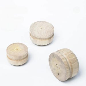 May include: Three circular wooden objects with a light tan, natural wood grain finish. Each piece features a distinct horizontal groove running around the center of its side, creating a spool-like shape with flat top and bottom surfaces.